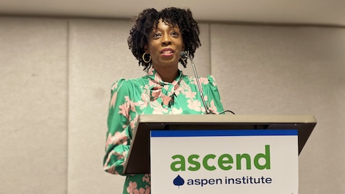 Vinice Davis of Imaginable Futures stands at a podium and is speaking. The podium has a sign that says: "Aspen Institute" and "Collaborative Action for Student Parents."