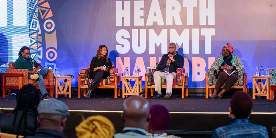 Four people sit on colorful chairs on a stage, with the phrase "Hearth Summit Nairobi" projected in the background.