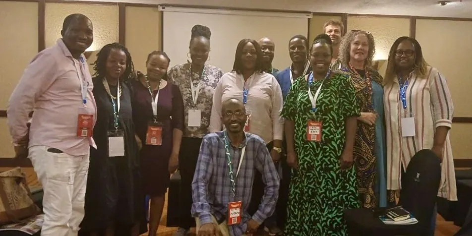 A group of people wearing red badges are standing and smiling in a conference room.