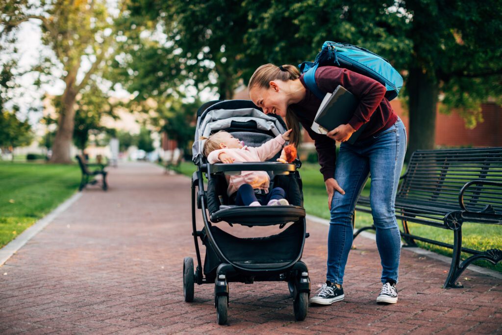 A mother and parent sits with her baby daughter on a university campus studying for a class. She is a hard working college student trying to earn her degree in education to improve her situation during difficult times.