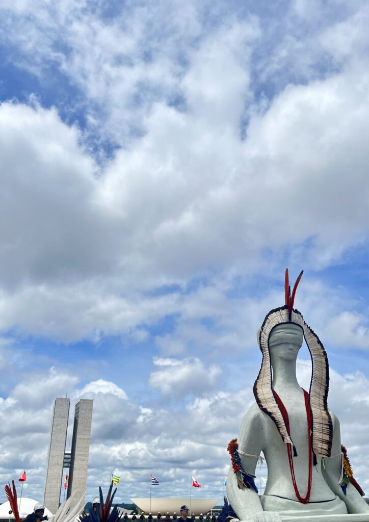 Justice statue wearing an Indigenous adornment in front of iconic Brasília building