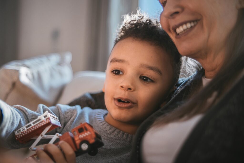 Young child holding firetruck toy leaning against older woman
