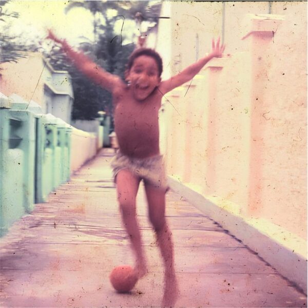 Childhood photo of Atila Roque expressing joy while ball in the streets of Brazil