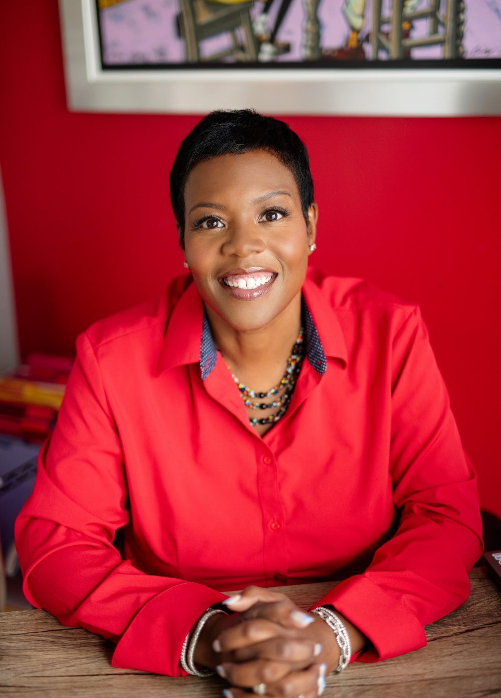Headshot of Kaya Henderson, board member of Imaginable Futures, sitting at a desk in a red shirt